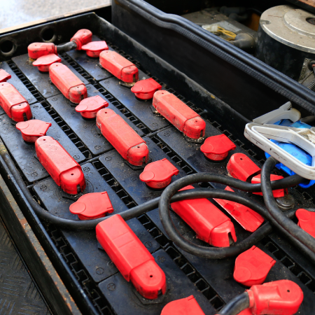 Close-up of a lead-acid battery with red caps and connected charging cable.