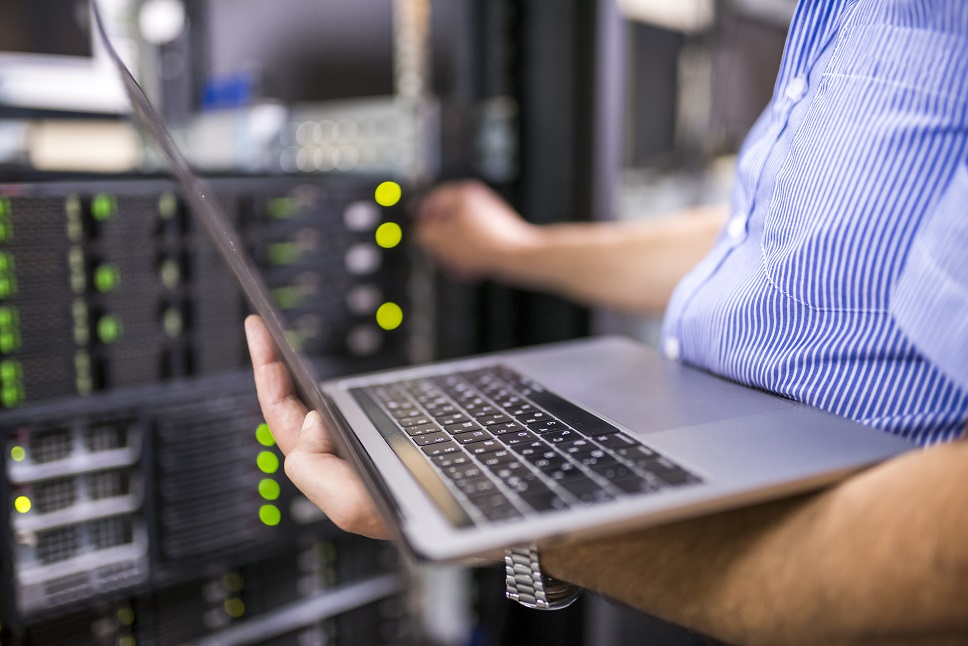 Technician with laptop managing servers in a data center, indicating network maintenance or setup.