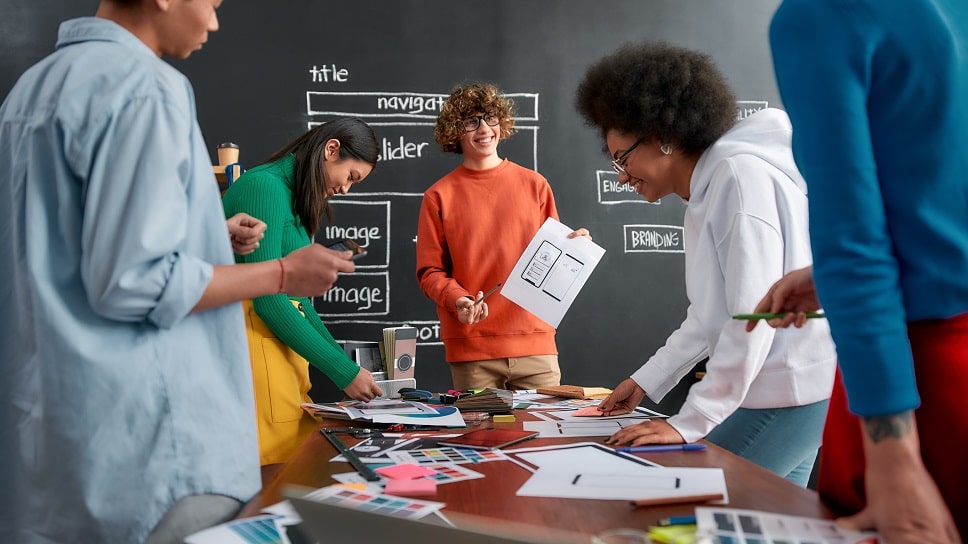 Creative team collaborating on web design project with color samples and layout sketches on a table.