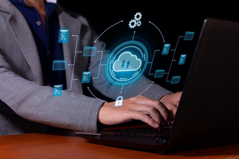 Professional in a blazer typing on a laptop with a virtual cloud computing interface with security and data icons floating above.