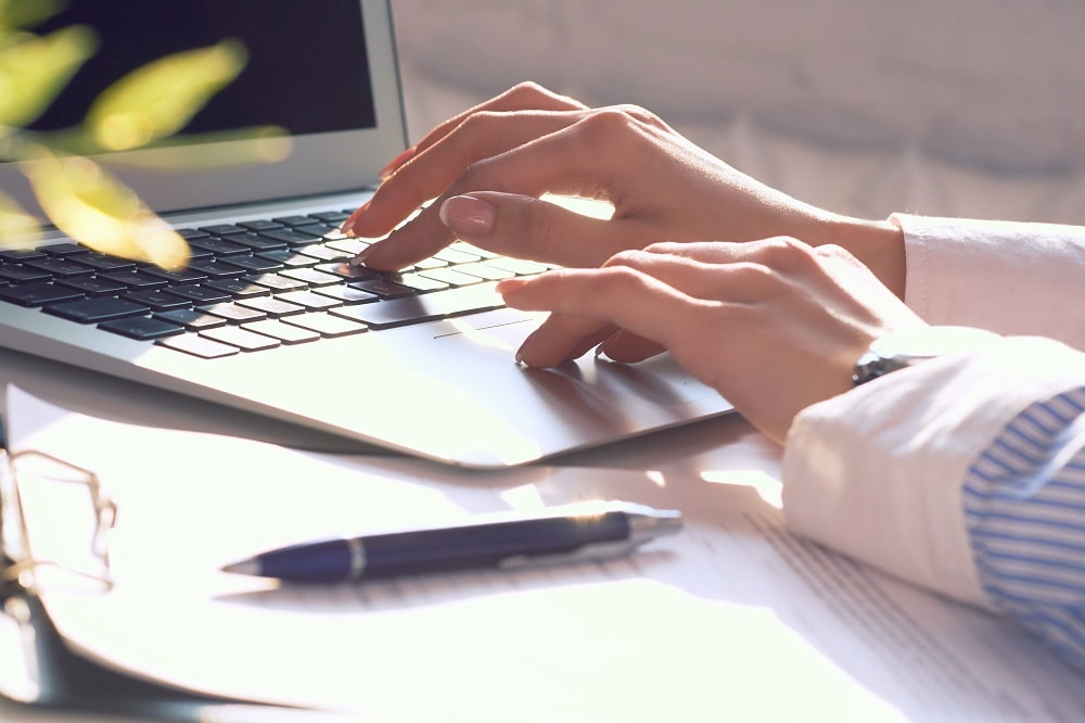 woman typing on computer with pen and paper to the side