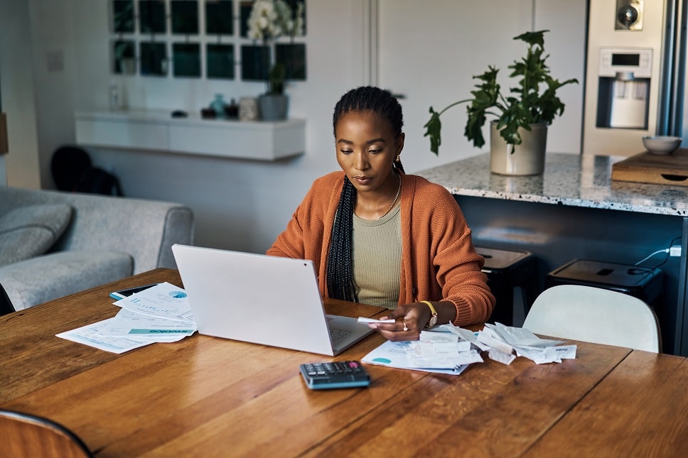 Focused woman budgeting finances with laptop and calculator at home.