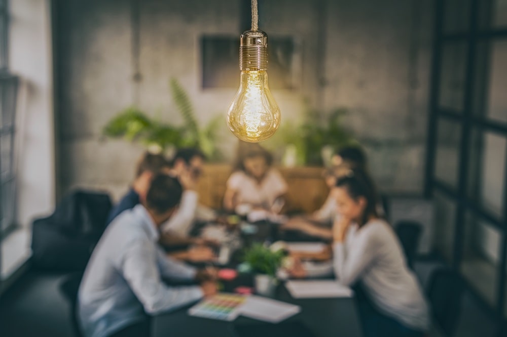 team brainstorming around a table with a lightbulb above them