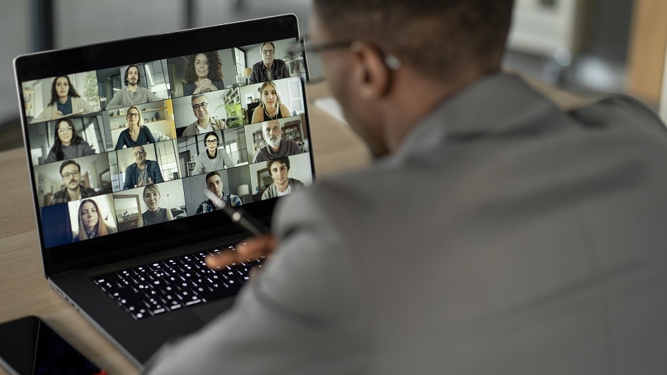 Business professional in a video conference call with multiple participants on a laptop screen, indicating remote teamwork.