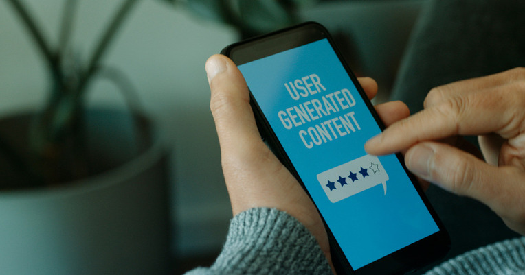 Person using smartphone displaying User Generated Content, highlighting the impact of customer reviews on ecommerce success