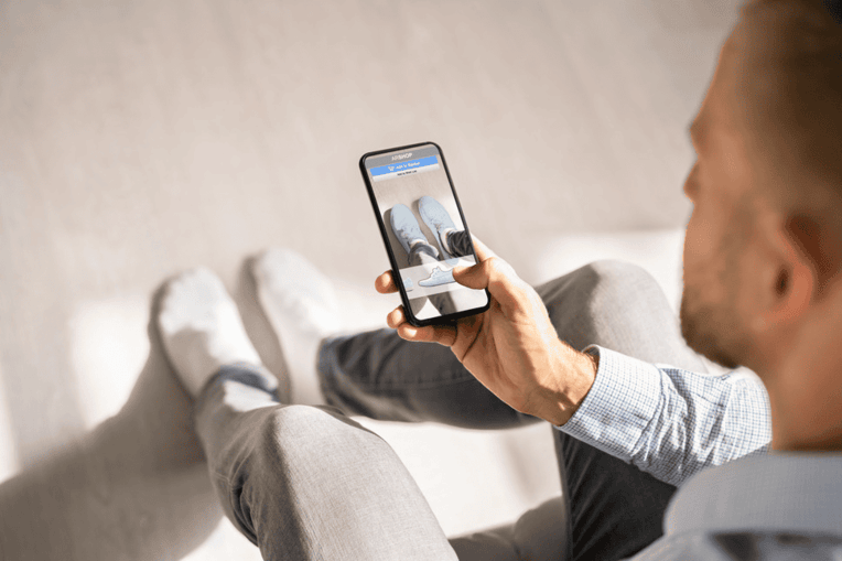Person using mobile device to shop for shoes online, showcasing interactive ecommerce content and virtual product experiences