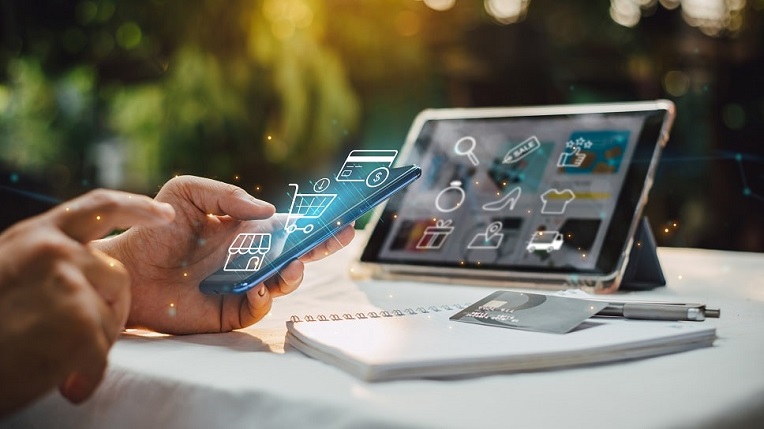 Person using a smartphone and tablet with digital shopping and business icons floating above, symbolizing e-commerce and online shopping solutions.
