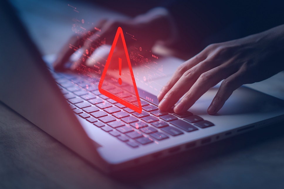 Hands typing on a laptop with a digital security alert symbol overlay.