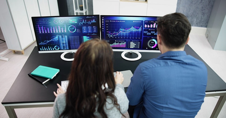 Two professionals analyzing data on computer screens with graphs, charts, and analytics for user experience insights.
