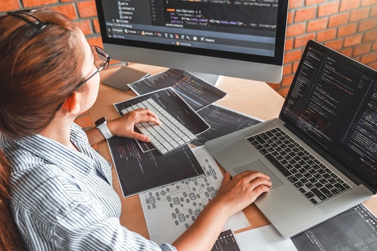 Female developer coding on multiple screens with programming languages displayed, in a modern tech workspace.