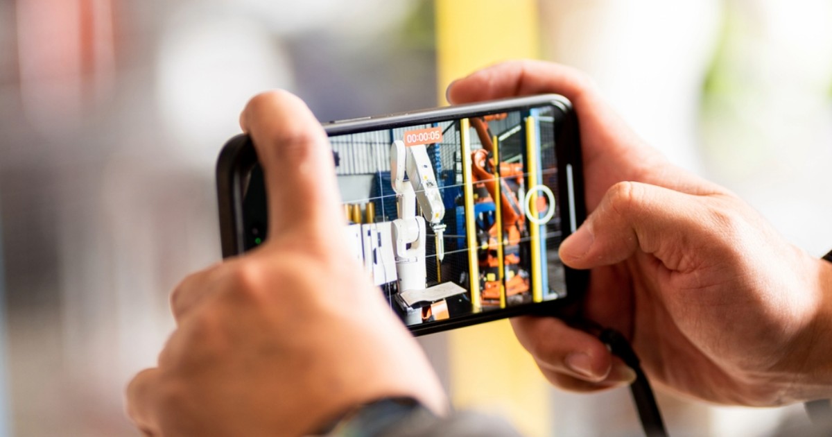 Worker using smartphone to record video of manufacturing process and industrial machinery for social media marketing success