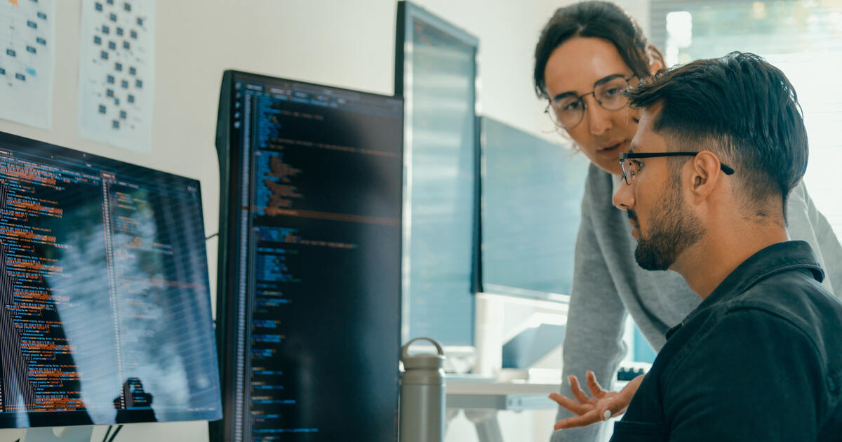 Developers reviewing code on monitors, collaborating on website production, UX design frameworks, and web development.