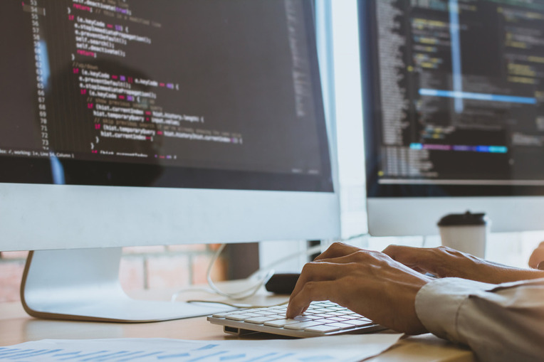 Developer coding using a computer with multiple monitors displaying lines of code on a mobile app development platform