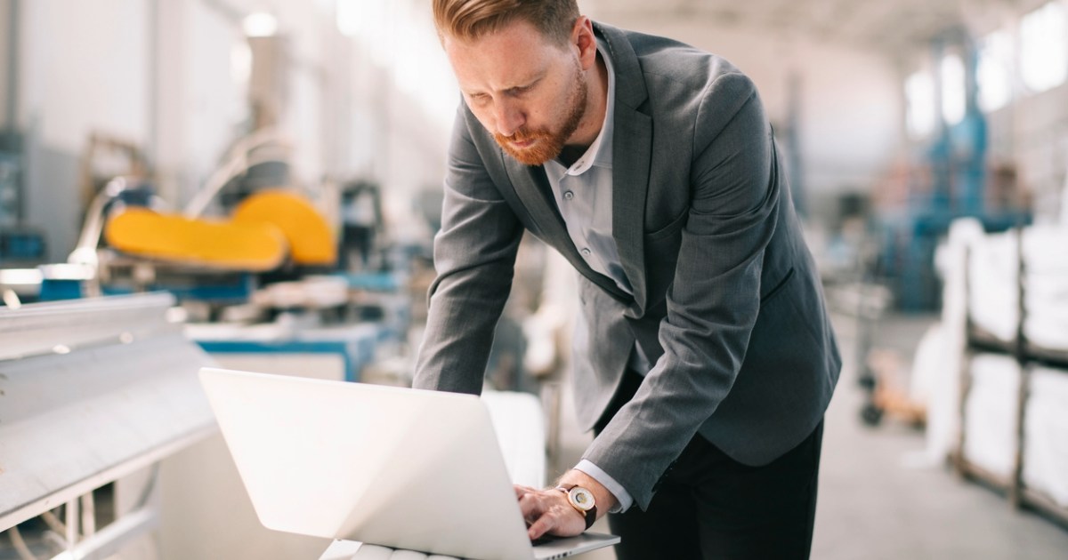 Business professional using a laptop inside a manufacturing facility, representing B2B operations and digital transformation