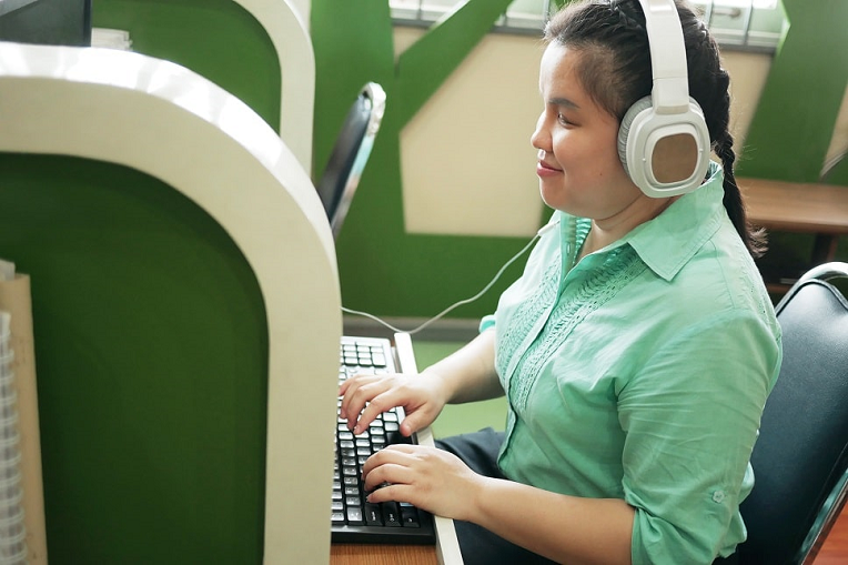 Woman sitting at a computer using headphones and other input devices for web accessibility