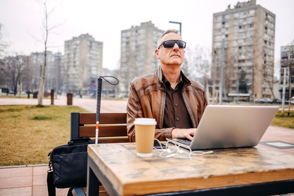 Visually impaired person using laptop outdoors, signifying business success with website accessibility agency services