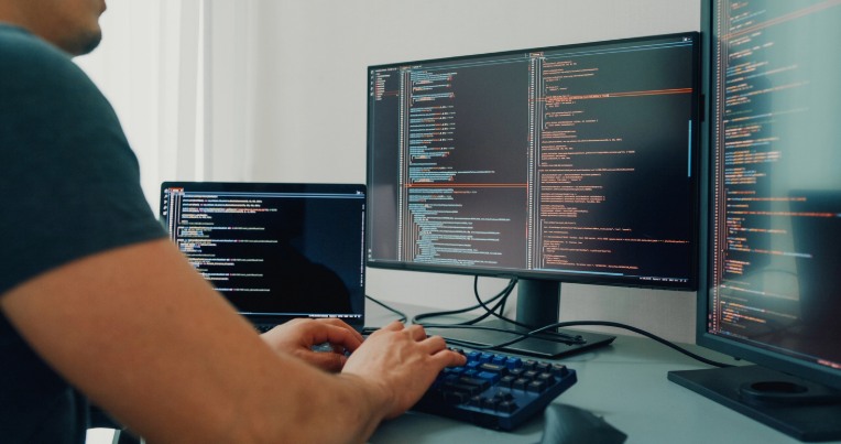 Developer working at a desk with multiple monitors displaying code for a website, highlighting front-end development services
