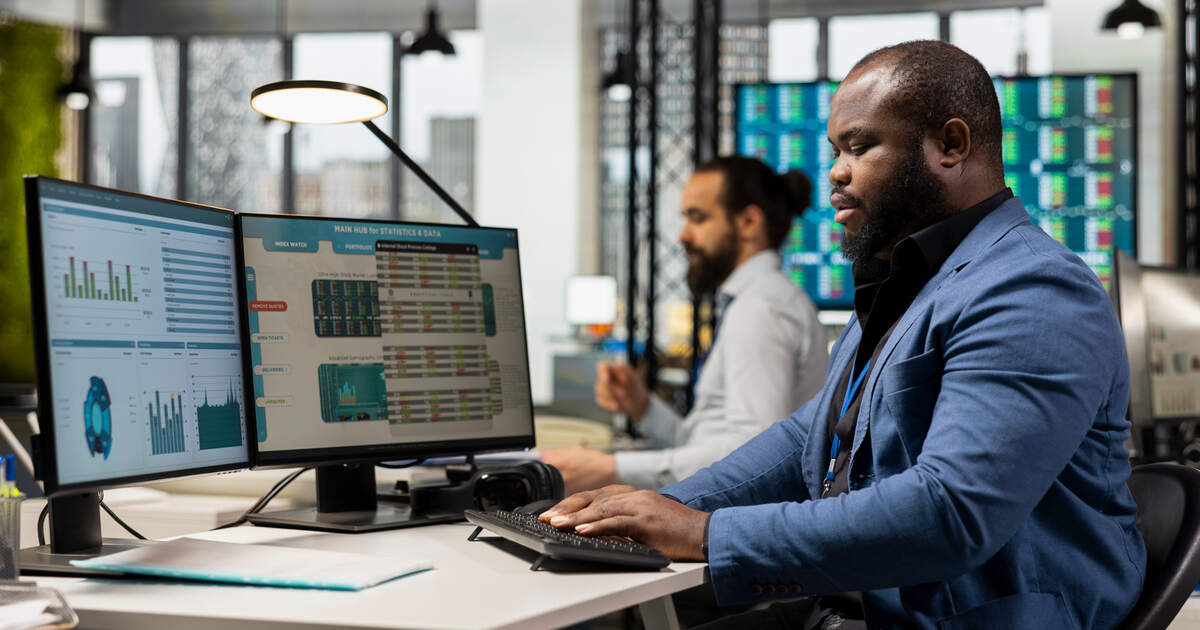 Professional monitoring Liferay analytics dashboards and reporting data across dual computer screens in an office.