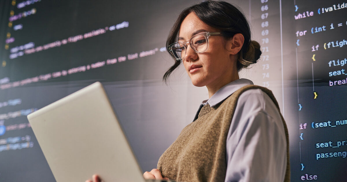 Developer reviewing code on a laptop with programming screens in the background, illustrating web development and coding.