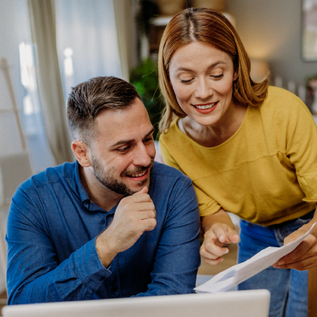 Smiling couple reviewing paperwork together at a laptop, showing digital marketing success for financial services