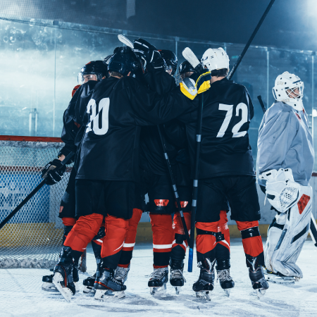 A group of hockey players in black jerseys celebrating on an ice rink with one player raising a hockey stick.