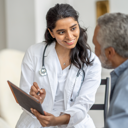 Smiling female doctor with a stethoscope consulting an elderly male patient while holding a digital tablet.